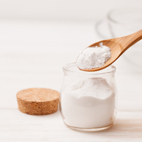 Natural baking soda powder in a glass jar with wooden spoon, commonly used in DIY skincare for gentle exfoliation, deep cleansing, and balancing skin